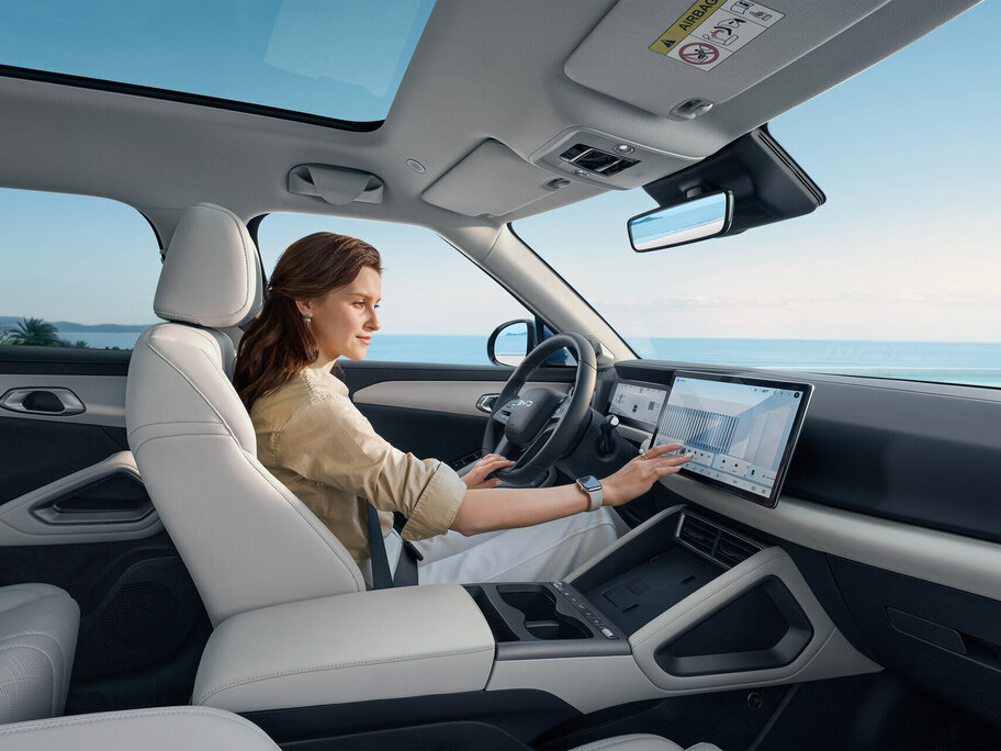 Person sitzt auf dem Fahrersitz eines Autos und berührt den großen Touchscreen in der Mittelkonsole