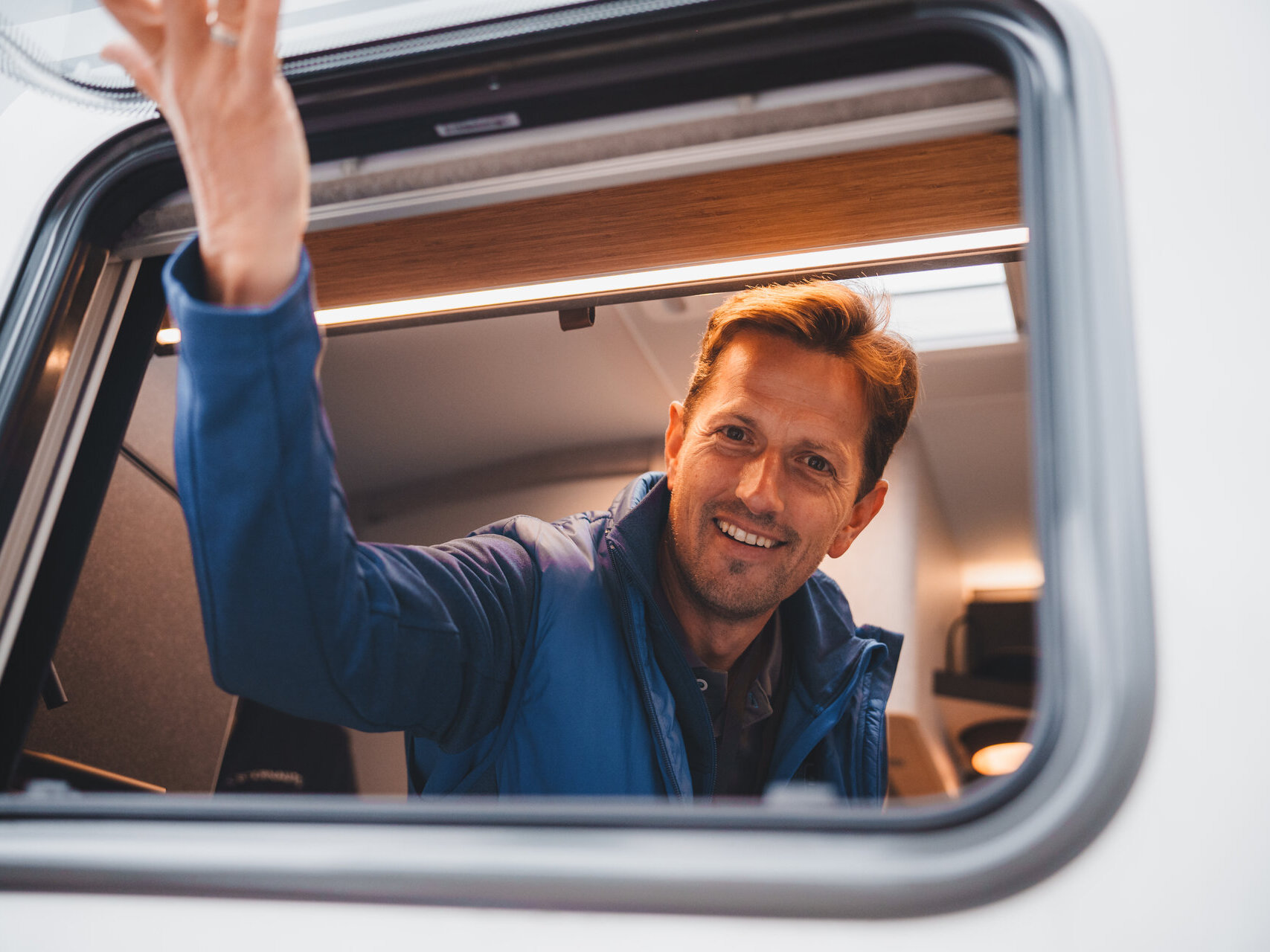 Heiko öffnet das Fenster von einem Wohnmobil und schaut heraus
