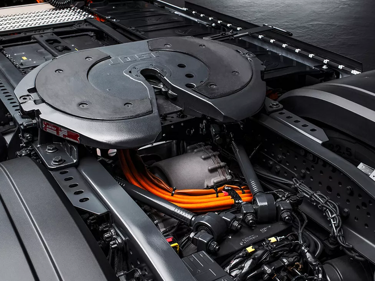 Nahaufnahme eines Lkw-Fahrgestells mit Schwerpunkt auf der Sattelkupplungsplatte und den sichtbaren orangefarbenen Stromkabeln, die auf einen Elektro- oder Hybrid-Lkw-Antriebsstrang hinweisen.