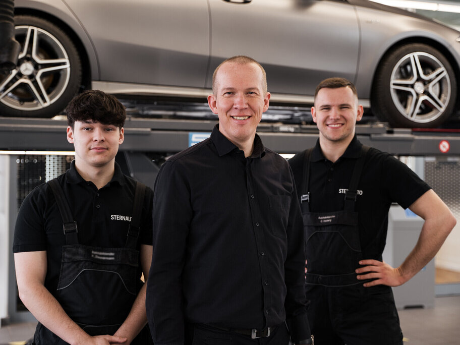 3 Mechaniker stehen vor Hebebühne mit Auto