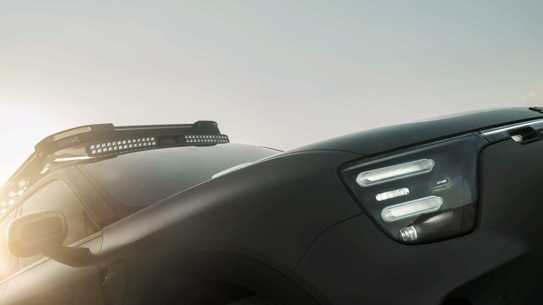 Nahaufnahme der Vorderseite eines modernen schwarzen smart mit eleganten Scheinwerfern und einer auf dem Dach montierten LED-Lichtleiste, wobei das Sonnenlicht die Szene aus dem Hintergrund beleuchtet.