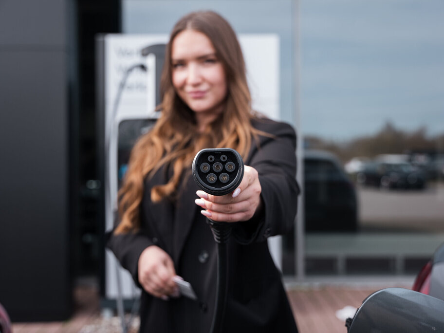 Eine Frau die einen E-Auto Ladestecker hoch hält