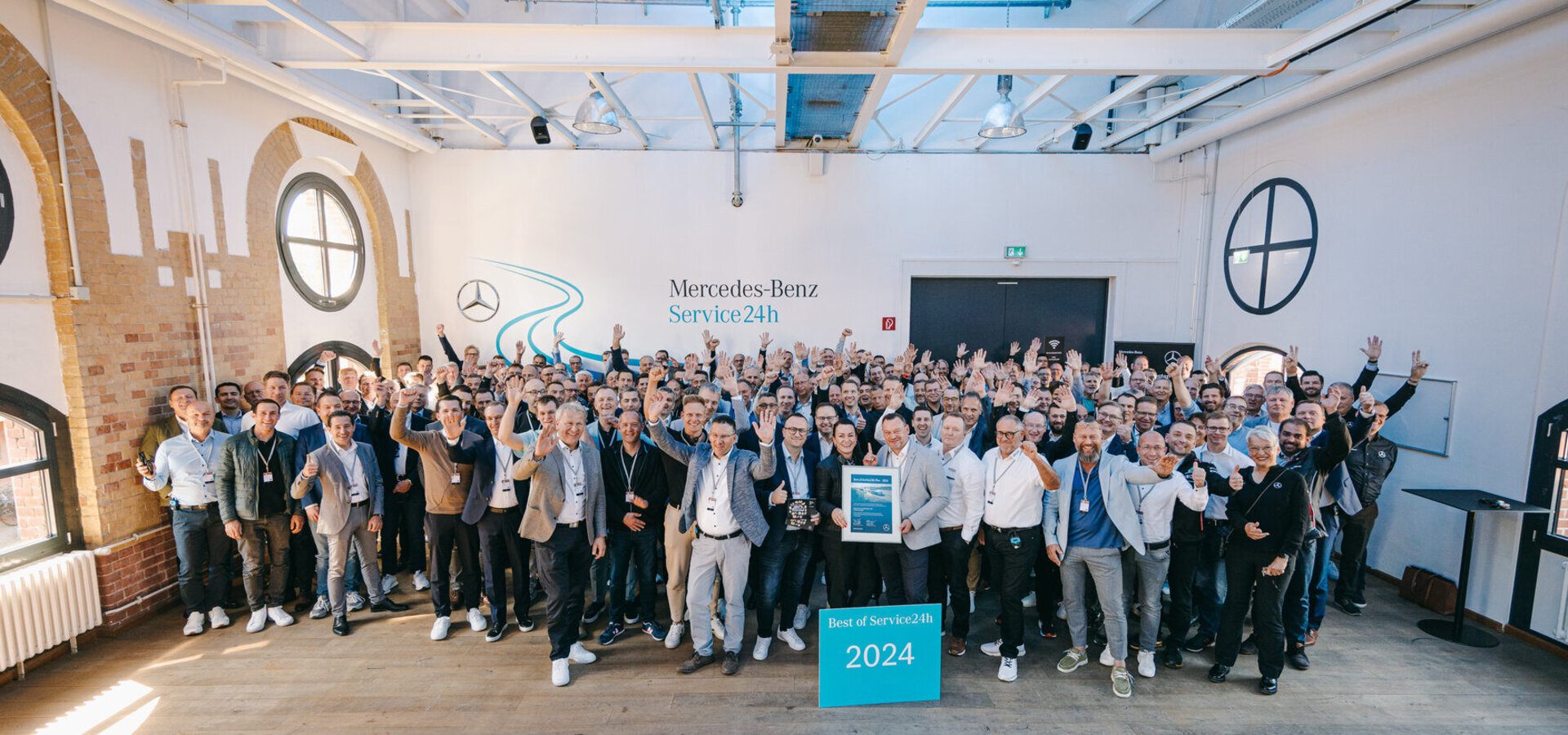Eine Gruppe von Menschen jubeln und stehen hinter einem Schild mit der Aufschrift "Best of Service24h 2024"