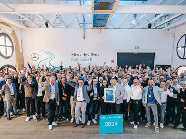 Eine Gruppe von Menschen jubeln und stehen hinter einem Schild mit der Aufschrift "Best of Service24h 2024"