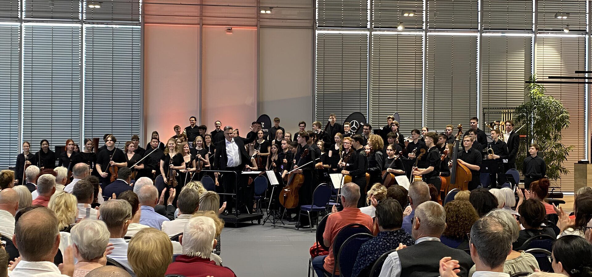Ein Orchester spielt vor einer sitzenden Menschenmenge in einem Autohaus