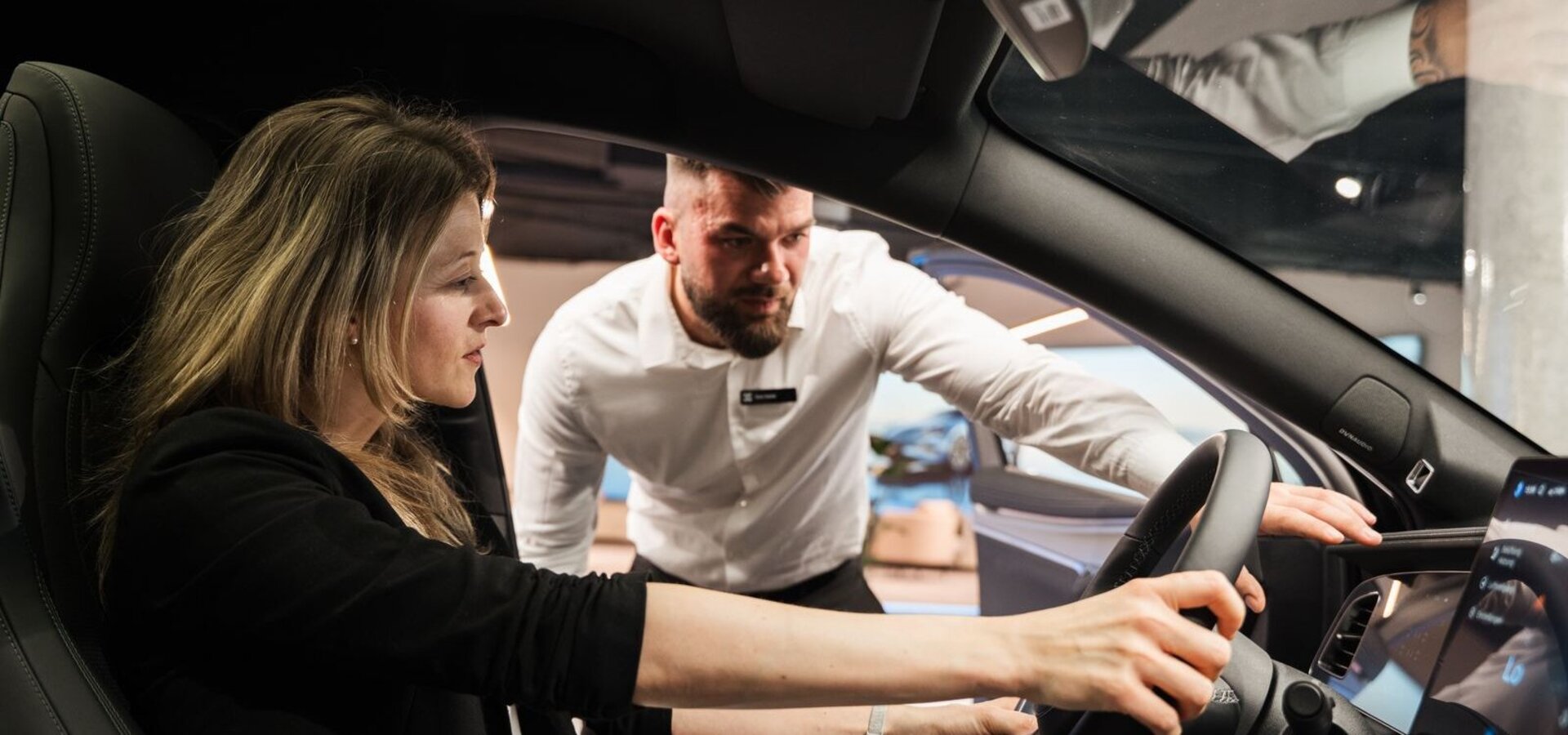 Eine Frau sitzt in einem BYD und hält das Lenkrad fest. Ein Mann steht neben dem Auto und erklärt ihr etwas