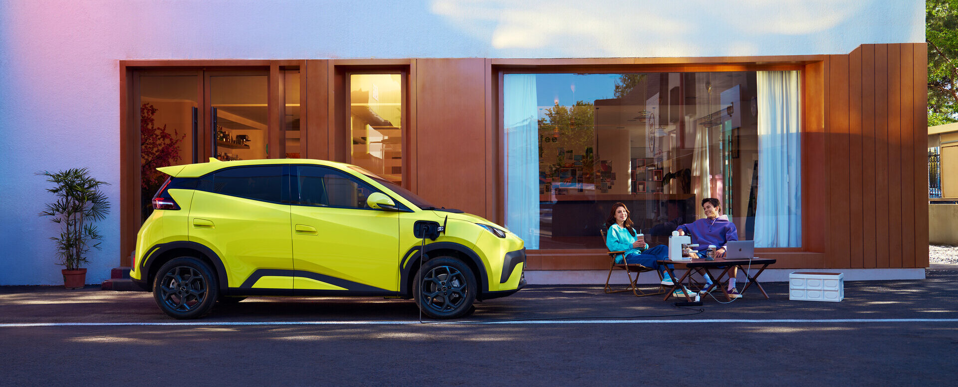 Der BYD Atto Dolphin Surf in lime green mit zwei Menschen die daneben Kaffee trinken