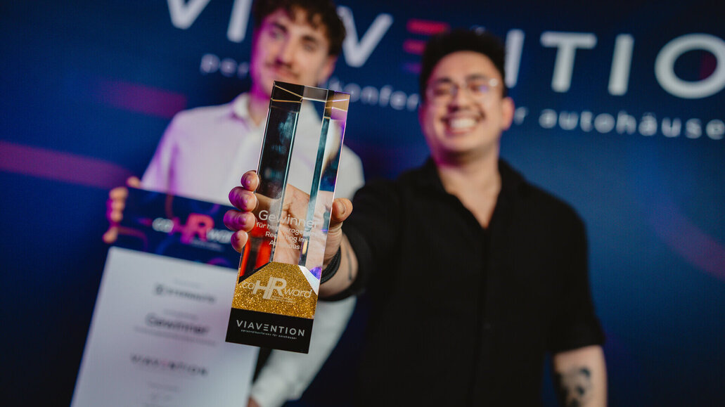 Zwei Personen halten eine gläserne Trophäe mit der Aufschrift 'HR Award' und 'VIAVENTION'. Im Hintergrund unscharfer Schriftzug 'VIAVENTION'.