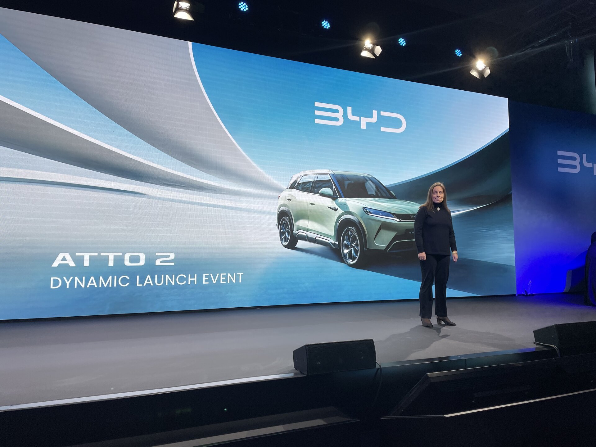 Person steht auf Bühne vor großer Leinwand mit Abbildung eines silbernen BYD ATTO 2 SUV und Text 'ATTO 2 DYNAMIC LAUNCH EVENT'.