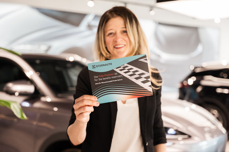 Eine Frau hält eine Karte hoch auf dem steht "Die Pole-Position ist bereits für Sie reserviert"