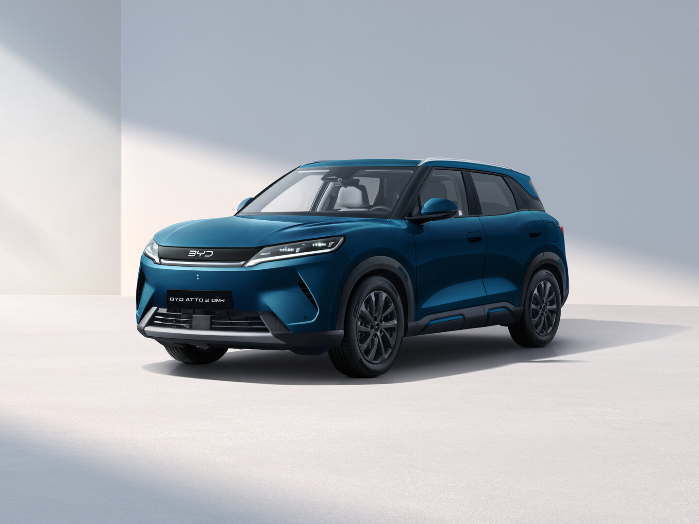 Blauer BYD ATTO 2 DM-i SUV steht in einem hellen, minimalistischen Raum mit Schatten an der Wand