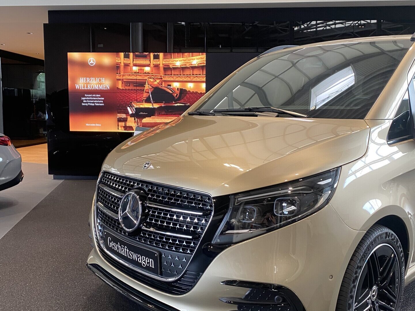 Ein Mercedes-Benz Van in der Farbe Champagner steht vor einem Bildschirm