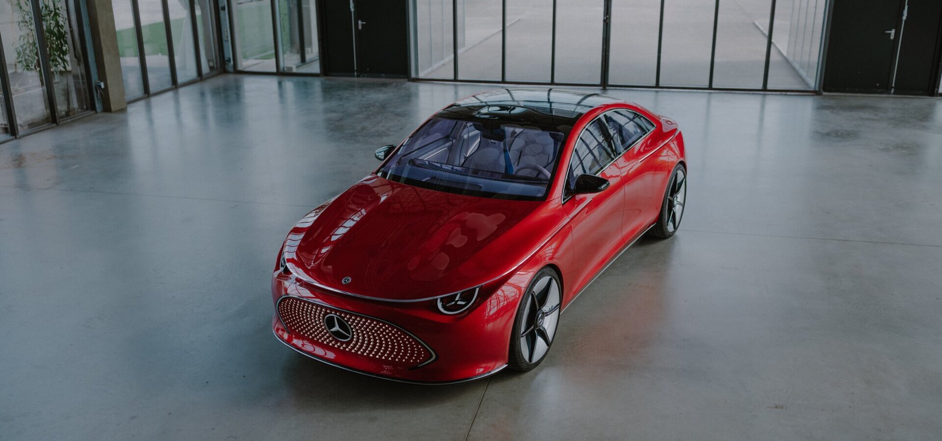 Ein schnittiges rotes Mercedes-Benz Elektroauto steht in einem geräumigen, modernen Ausstellungsraum mit Glaswänden, großen Fenstern und Türen.