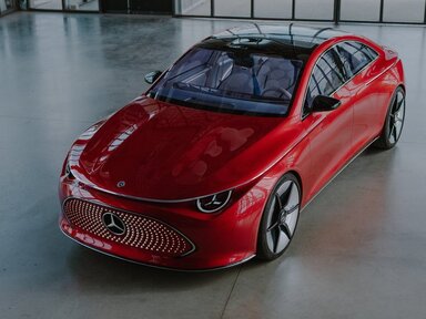 Ein schnittiges rotes Mercedes-Benz Elektroauto steht in einem geräumigen, modernen Ausstellungsraum mit Glaswänden, großen Fenstern und Türen.