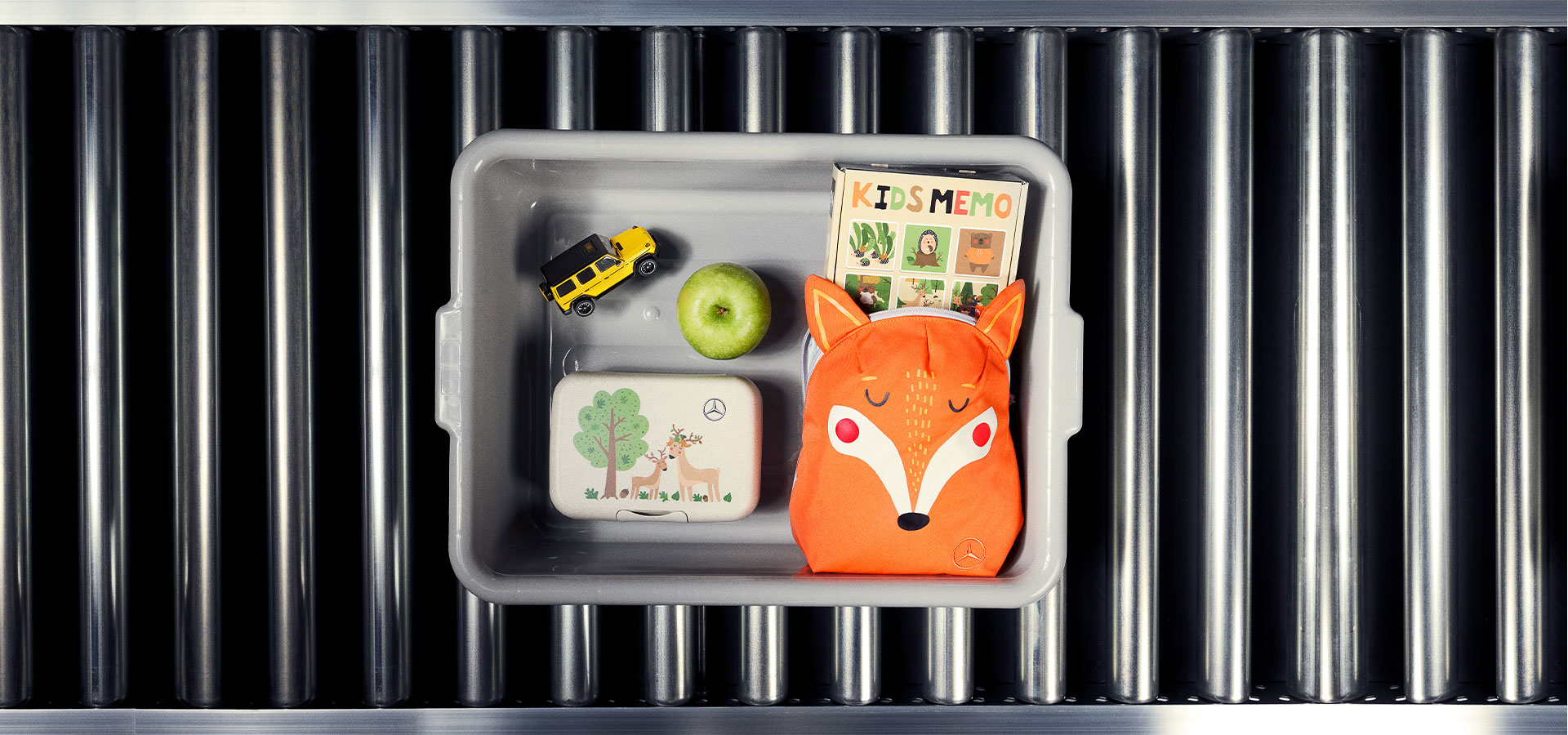 Offener grauer Lunchbox mit grünem Apfel, orangefarbenem Fuchsmotiv-Rucksack, gelbem Spielzeugauto und Memo-Kartenspiel mit der Aufschrift 'KIDS MEMO'.