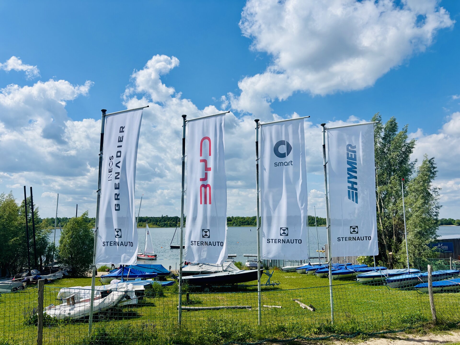 Vier Fahnen mit den Markenlogos INEOS Grenadier, BYD, smart und Hymer